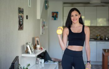 Smiling woman in activewear lifting dumbbells at home for a healthy lifestyle.