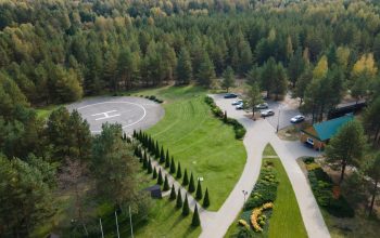 Aerial shot of a forest with a helipad, parking area, and landscaped gardens.